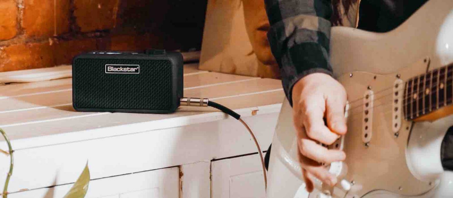 A Blackstar Beam Mini compact amp sitting on a modern wooden desk next to a laptop and an electric guitar, highlighting its small portable size.