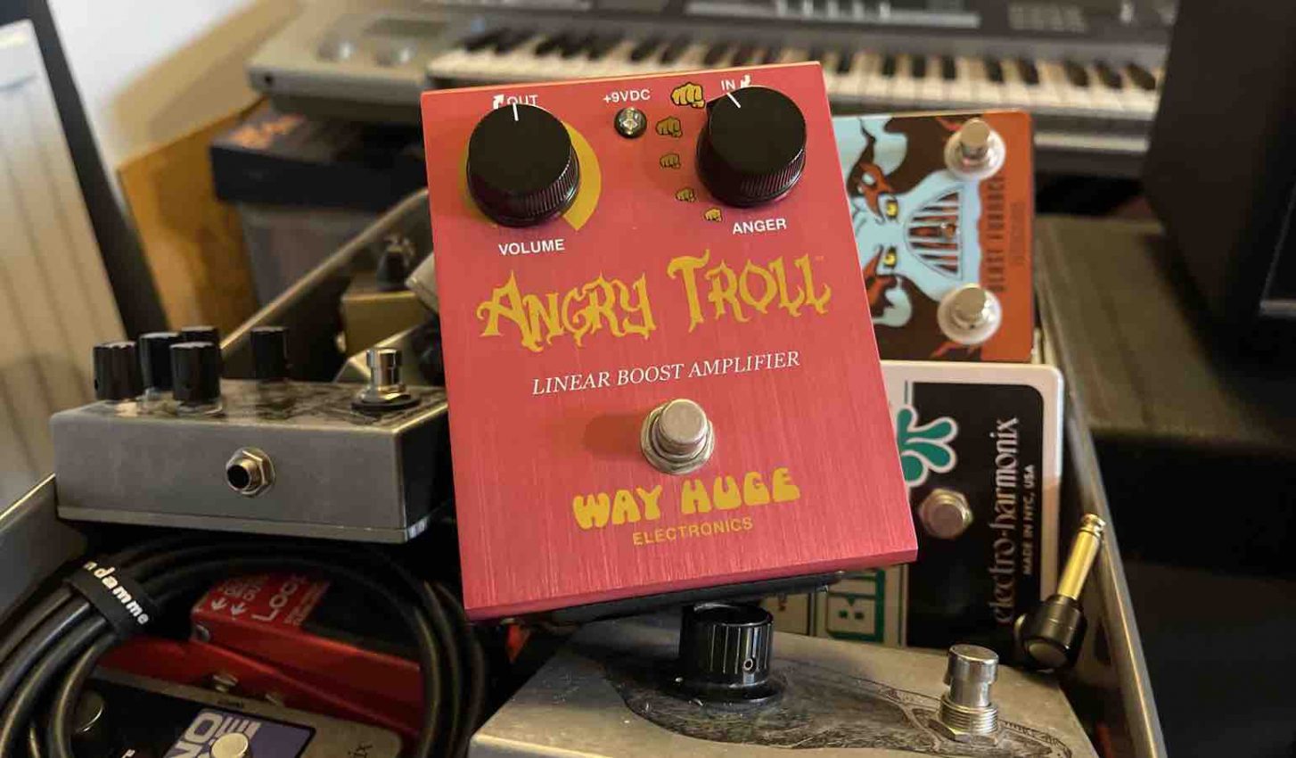 A vibrant red Way Huge Angry Troll boost pedal featuring two black knobs (Volume and Anger) and a metallic footswitch, set against a clean background to highlight its rugged aluminum chassis and iconic "Fists of Fury" graphic.