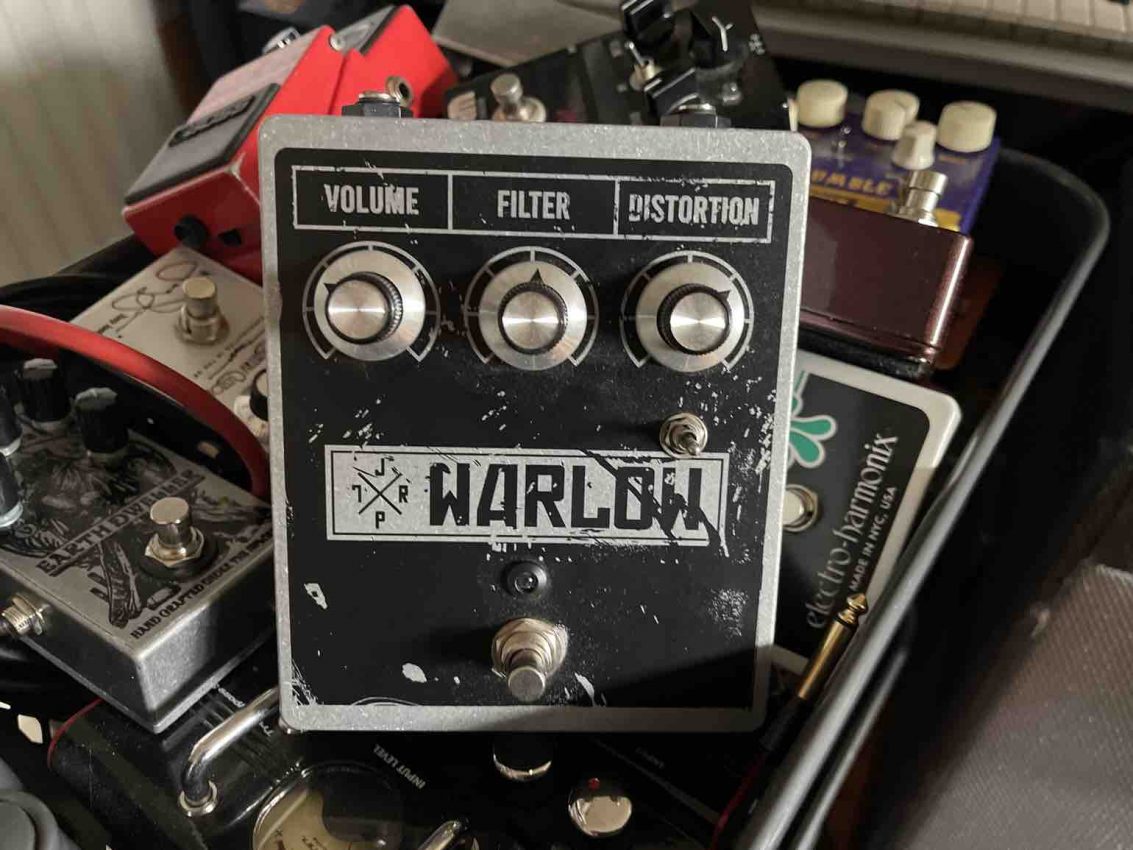 Top-down view of the JPTR FX Warlow fuzz pedal, featuring its boutique "fuzz monstrosity" artwork, oversized control knobs, and the signature three-way filter toggle switch on a rugged metal chassis.