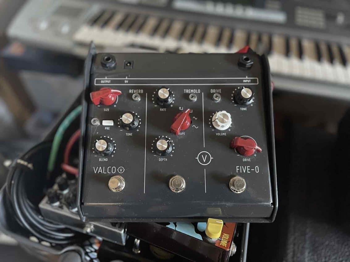 A top-down view of the Valco Five-O multi-effects pedal featuring a large wedge-shaped grey metal enclosure, top-mounted jacks, three independent footswitches for Drive, Tremolo, and Reverb, and a unique "PRE" routing button.