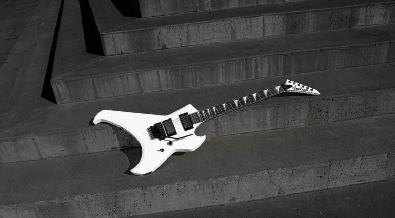 A pointed, angular offset-body Jackson electric guitar in a striking Snow White finish. The instrument features a black ebony fingerboard with pearloid sharkfin inlays, a black Floyd Rose double-locking tremolo system, and a streamlined layout with a single volume control.
